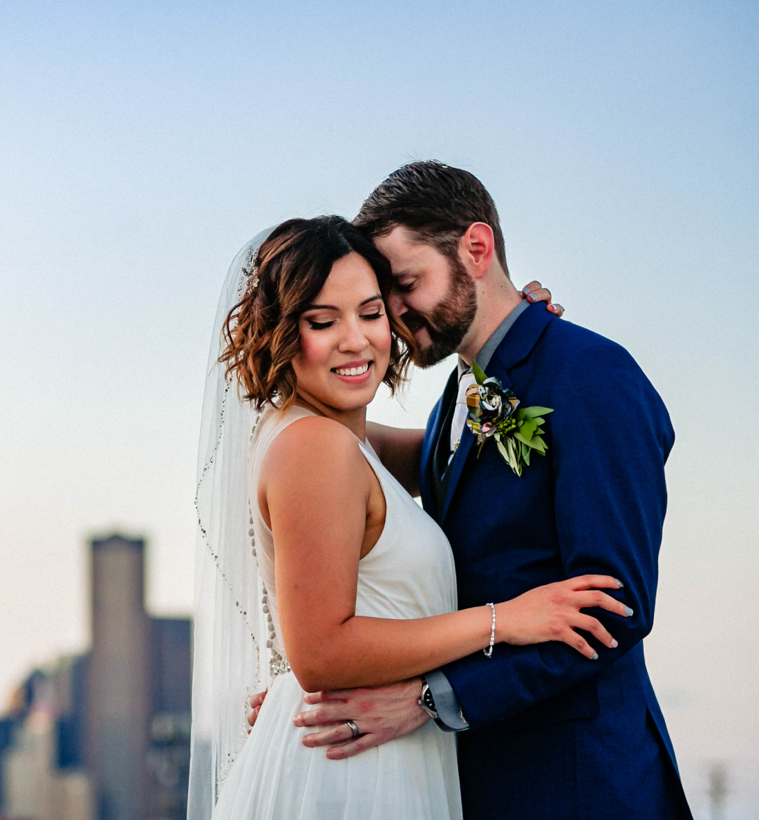 Newlyweds embracing outdoors with a city skyline behind them